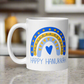 This ceramic glossy coffee cup says Happy Hanukkah and features a blue and yellow boho rainbow with a heart.