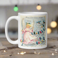 This ceramic glossy coffee mug features a retro Midcentury Christmas illustration of an angel dressed in pink directing blue, yellow and pink songbirds. At the top it says Merry Christmas HONEY