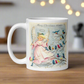 This ceramic glossy coffee mug features a retro Midcentury Christmas illustration of an angel dressed in pink directing blue, yellow and pink songbirds. At the top it says Merry Christmas HONEY