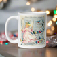 This ceramic glossy coffee mug features a retro Midcentury Christmas illustration of an angel dressed in pink directing blue, yellow and pink songbirds. At the top it says Merry Christmas HONEY