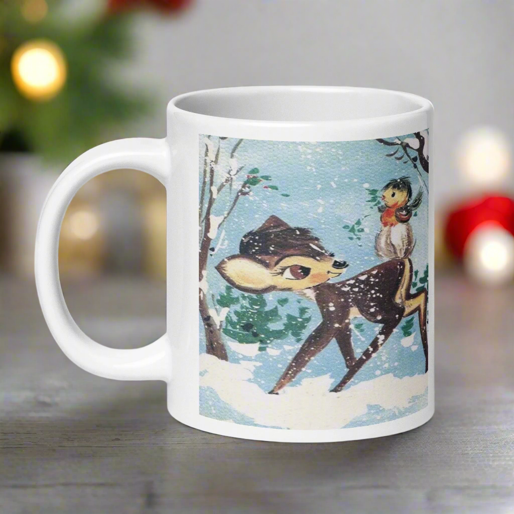 This glossy ceramic coffee cup features a retro woodland style Christmas winter illustration of a baby deer in the snow with a cute red and brown bird perched on her tail.