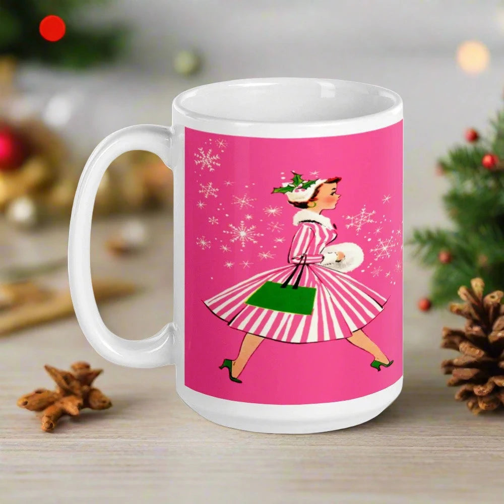 This ceramic glossy mug features a vintage Christmas illustration of a retro Midcentury housewife dressed in a pink and white striped dress with a green purse and heels. The background is pink and there are snowflakes. 