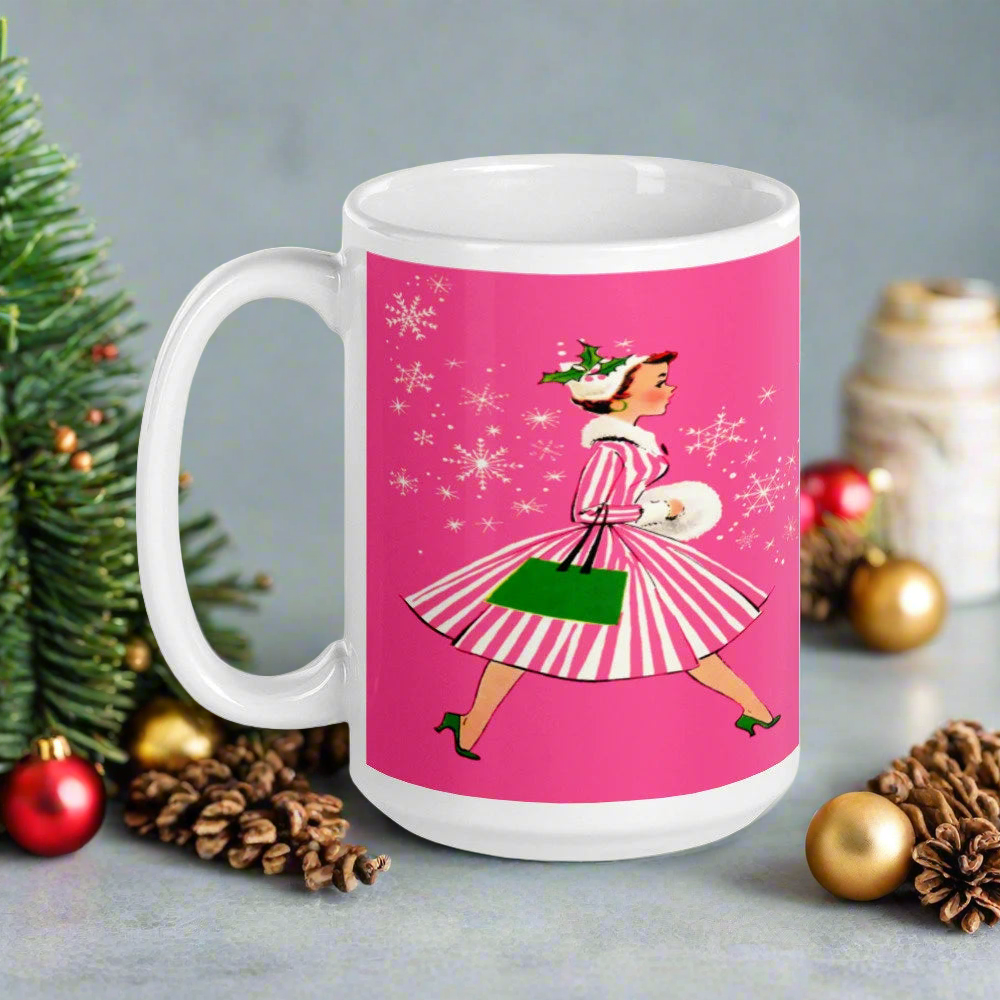 This ceramic glossy mug features a vintage Christmas illustration of a retro Midcentury housewife dressed in a pink and white striped dress with a green purse and heels. The background is pink and there are snowflakes. 