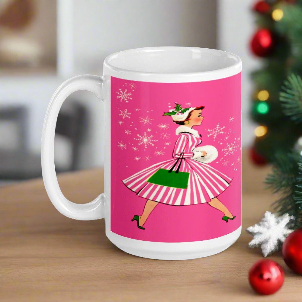 This ceramic glossy mug features a vintage Christmas illustration of a retro Midcentury housewife dressed in a pink and white striped dress with a green purse and heels. The background is pink and there are snowflakes. 