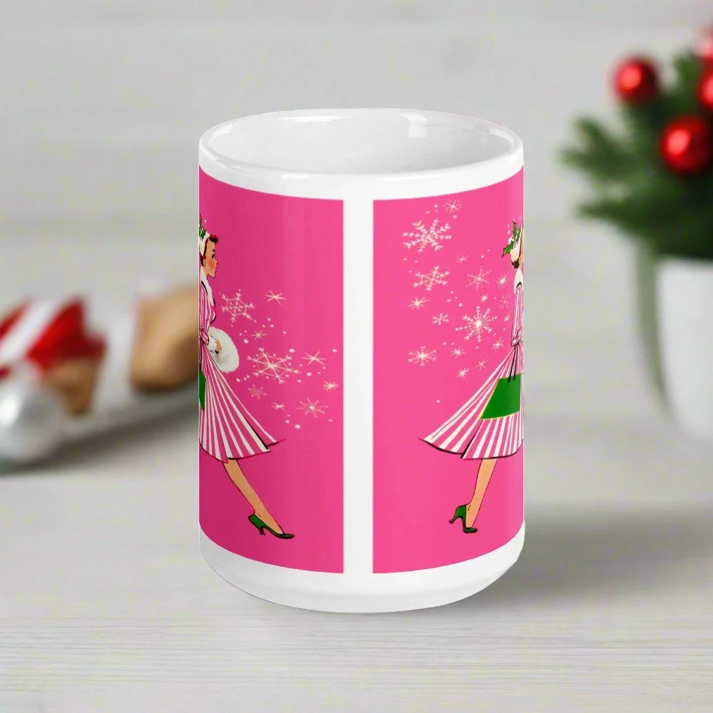 This ceramic glossy mug features a vintage Christmas illustration of a retro Midcentury housewife dressed in a pink and white striped dress with a green purse and heels. The background is pink and there are snowflakes. 