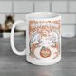 This glossy ceramic coffee mug features a retro vintage Halloween illustration that says Halloween with trees with spooky cute faces and orange leaves, with a jack o lantern in the middle and a black cat sleeping on the pumpkin.