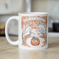 This glossy ceramic coffee mug features a retro vintage Halloween illustration that says Halloween with trees with spooky cute faces and orange leaves, with a jack o lantern in the middle and a black cat sleeping on the pumpkin.