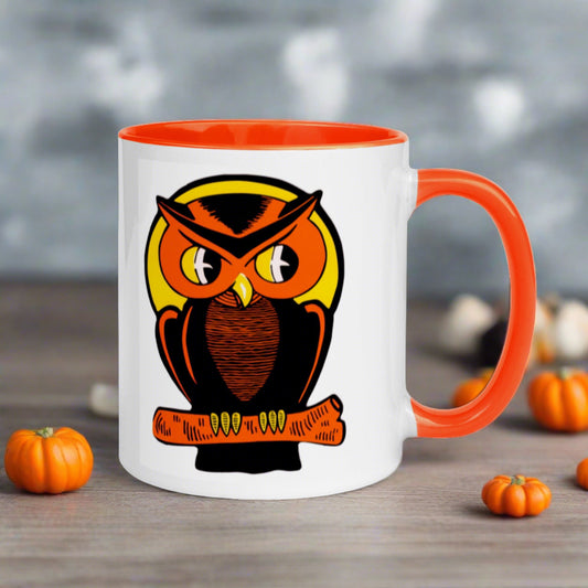 This glossy ceramic mug features a retro Halloween print of an orange owl perched on an orange branch with a yellow moon behind his head. The handle and inside of the mug is lined in orange.