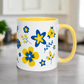 This ceramic glossy mug has a yellow handle and interior. The artwork features blue and yellow Ukranian country flowers.