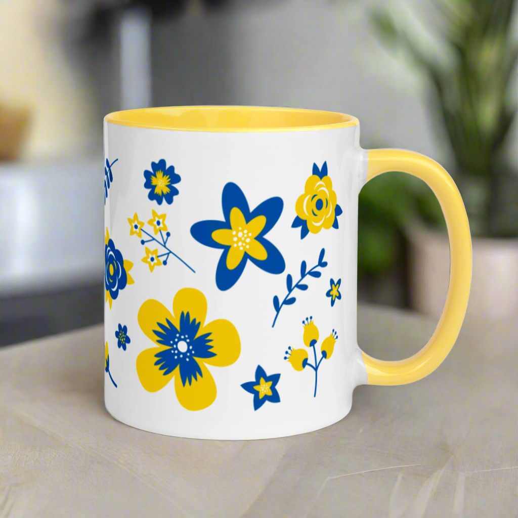 This ceramic glossy mug has a yellow handle and interior. The artwork features blue and yellow Ukranian country flowers.