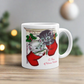 This white ceramic glossy coffee mug features two adorable kittens in red stockings at a Christmas mantle. The print is retro kitsch and says A Pair of Warm Wishes.