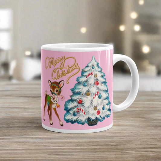 This ceramic glossy mug has a Mid Century retro Christmas print of an adorable deer with a candy cane in mouth and white christmas tree outlined in teal. The words Merry Christmas are gold and there is a pink background of the whole design.