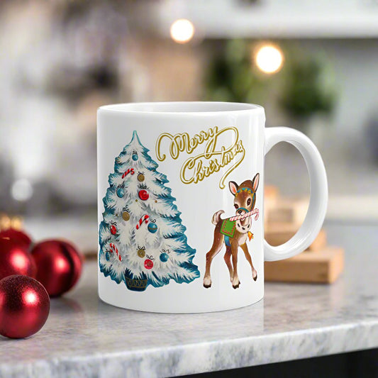 This ceramic glossy mug features retro midcentury artwork of a reindeer holding a candy cane in her mouth and a white Christmas tree outlined in blue. There is gold lettering that says Merry Christmas.