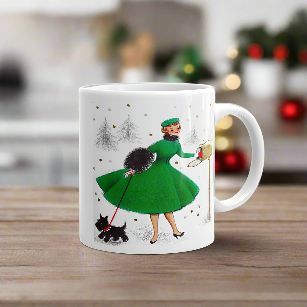 This ceramic glossy coffee mug features a midcentury retro Christmas illustration of a woman dressed in a green dress with a green hat, a black muff and red and white striped glove. She is walking her little black scottie and reaching into her mailbox. 