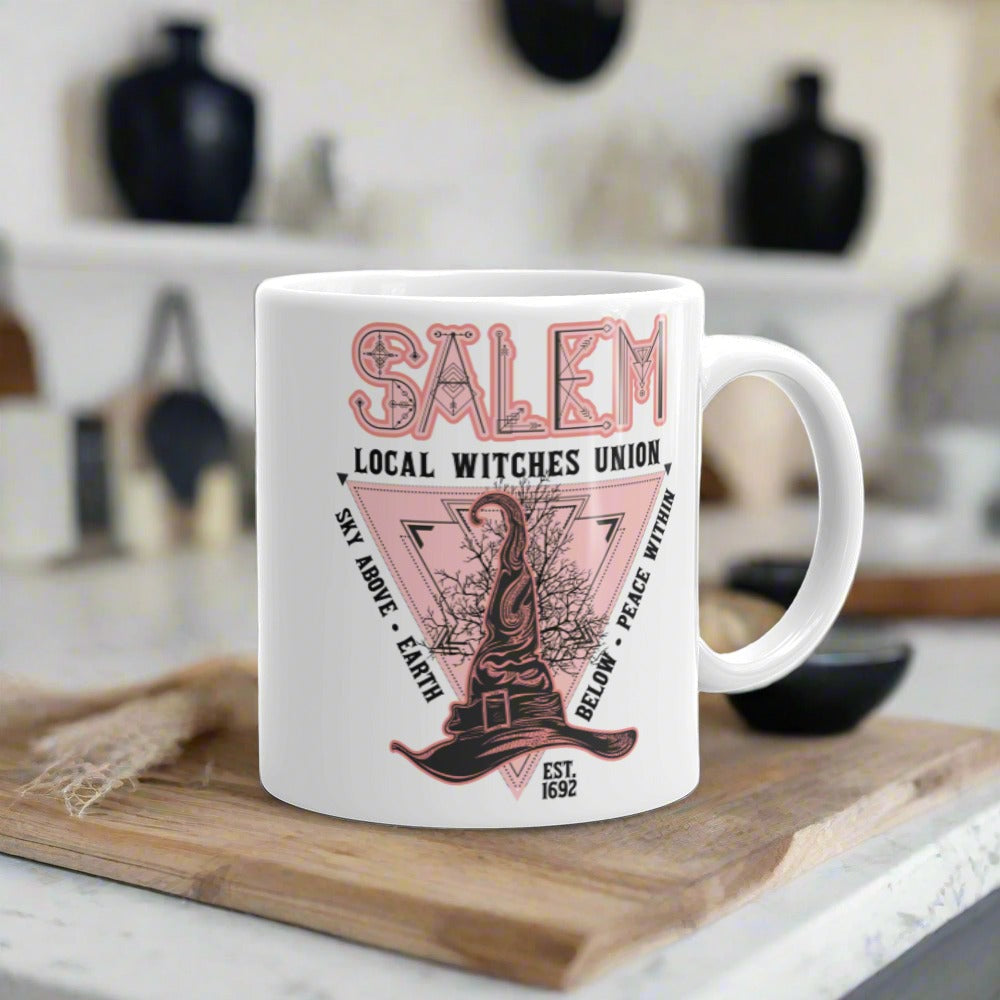 This ceramic glossy mug says Salem Local Witches Union and features a pointy pink and black witch's hat. It says Sky Above Earth Below Peace Within Est 1692.