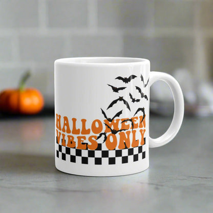 This ceramic glossy Halloween mug features a retro style print that says Halloween Vibes Only. There are flying bats and a black and white checkered print at the bottom.