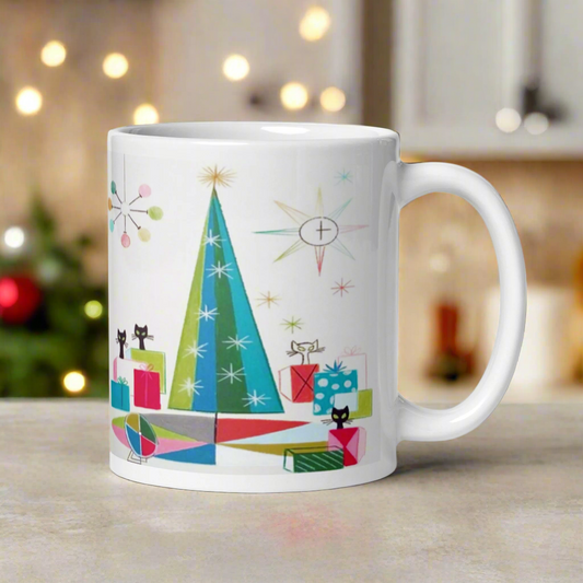 This ceramic glossy Christmas coffee mug features an atomic Midcentury illustration of cats peeking out from behind presents around a Christmas tree. There is a colorful round rug, light projector, clock and chandelier all in atomic era style.