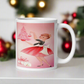 This glossy ceramic coffee mug features a midcentury retro Christmas illustration of a woman dressed in black and pink holding a small pink Christmas and ornament. There are a couple of presents and a pink background.