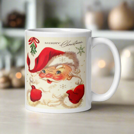 This ceramic glossy coffee mug features a midcentury retro Christmas illustration of Santa smiling under a sprig of mistletoe. It says Merry Christmas abovehis head and there are snowflakes.