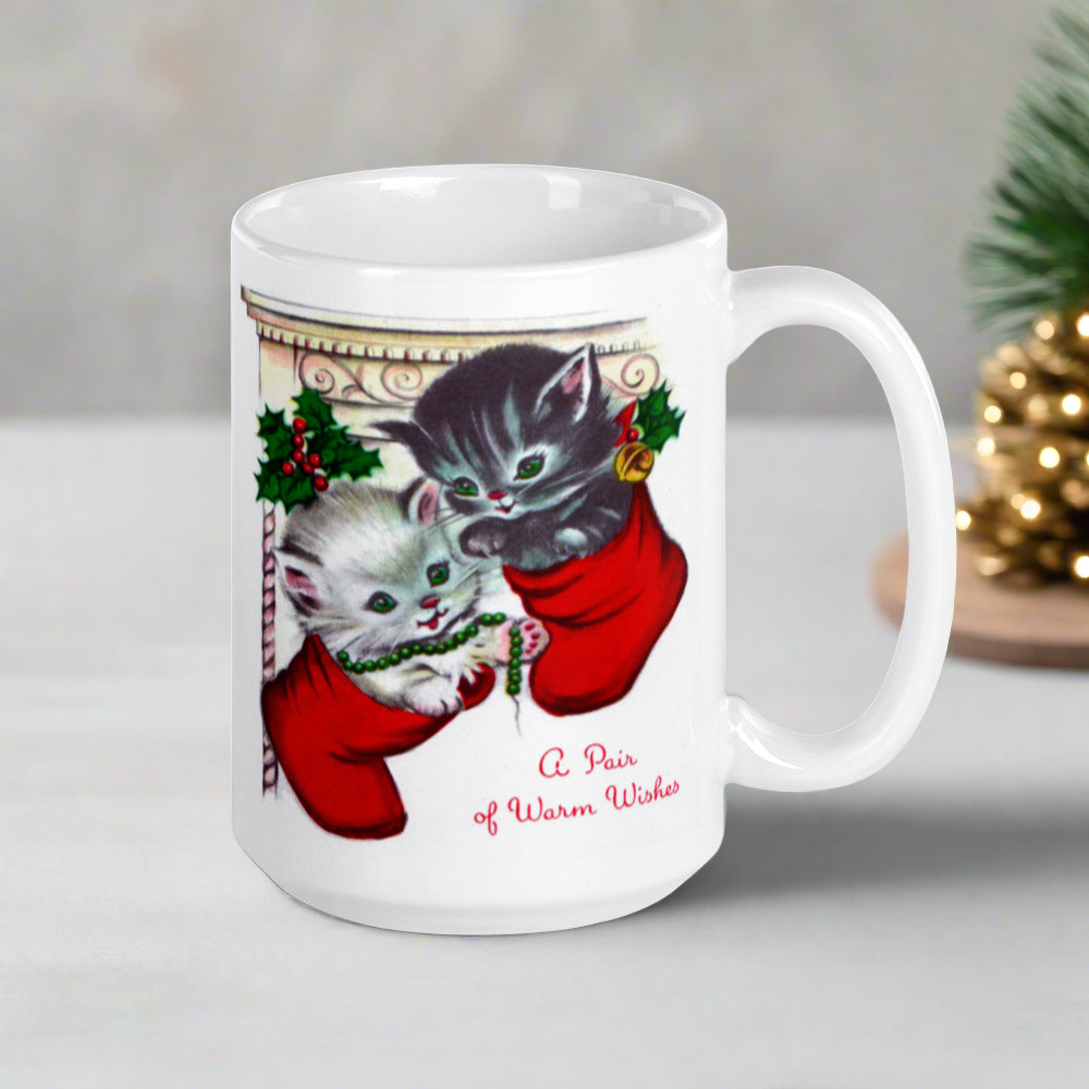 This white ceramic glossy coffee mug features two adorable kittens in red stockings at a Christmas mantle. The print is retro kitsch and says A Pair of Warm Wishes.