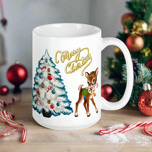 This ceramic glossy mug features retro midcentury artwork of a reindeer holding a candy cane in her mouth and a white Christmas tree outlined in blue. There is gold lettering that says Merry Christmas.