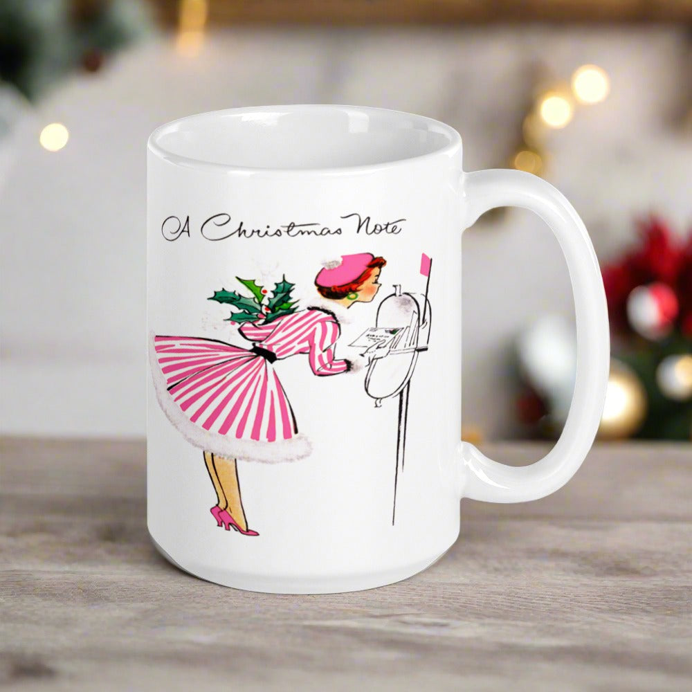 This ceramic glossy coffee mug features a retro vintage Christmas illustration of a woman holding a holly plant checking her mailbox. She is wearing a pink hat, pink and white striped dress, and pink heels. The illustration says A Christmas Note.