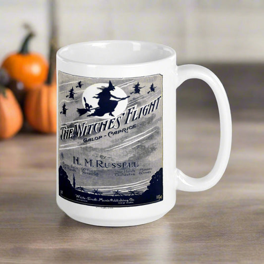 This glossy ceramic coffee mug features vintage Halloween artwork from a sheet music cover titled The Witches Flight featuring flying witches on broomsticks through the night sky with a full moon.