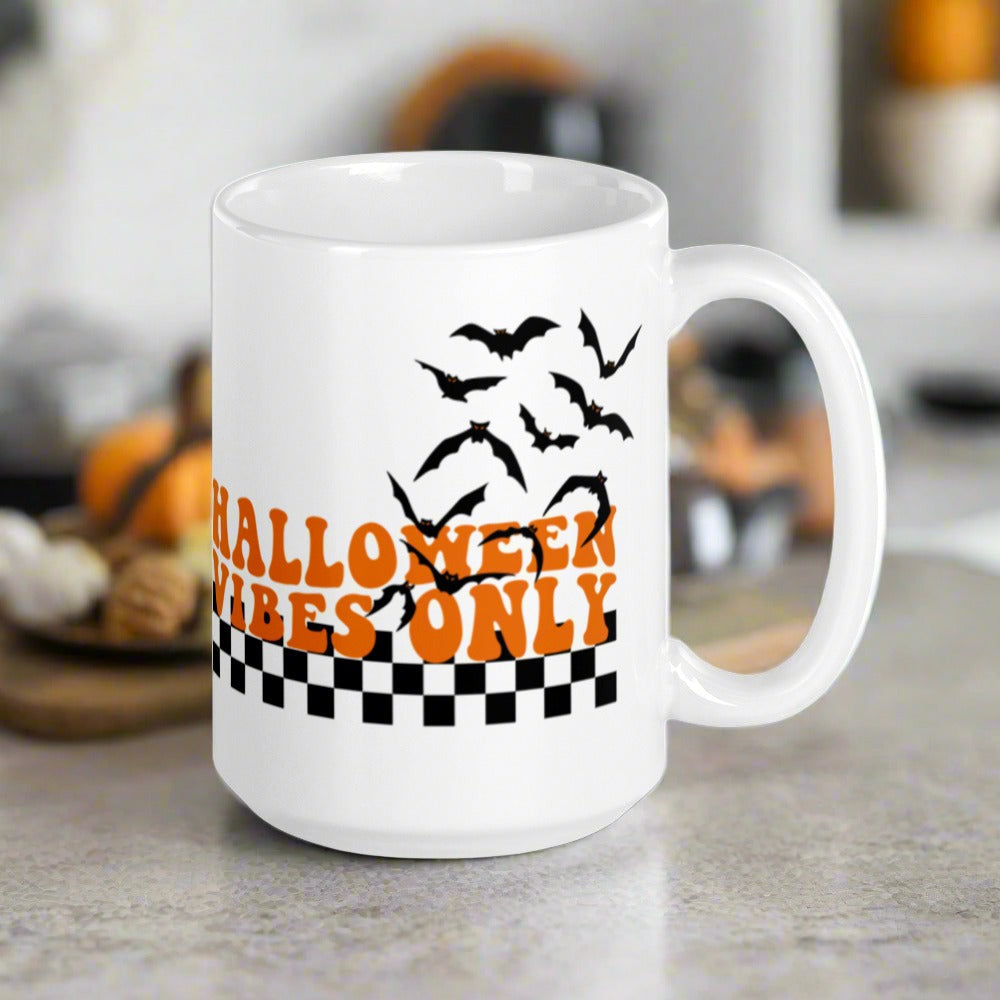 This ceramic glossy Halloween mug features a retro style print that says Halloween Vibes Only. There are flying bats and a black and white checkered print at the bottom.