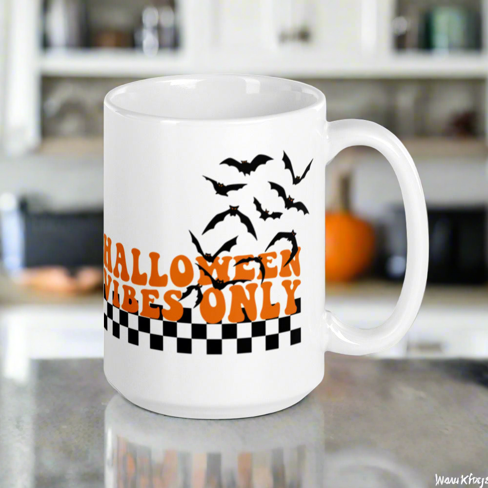 This ceramic glossy Halloween mug features a retro style print that says Halloween Vibes Only. There are flying bats and a black and white checkered print at the bottom.