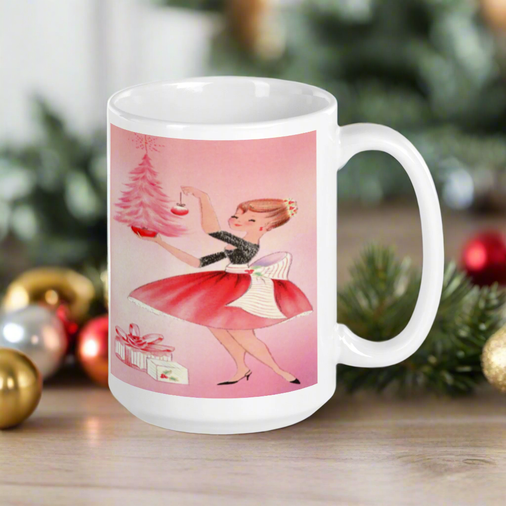 This glossy ceramic coffee mug features a midcentury retro Christmas illustration of a woman dressed in black and pink holding a small pink Christmas and ornament. There are a couple of presents and a pink background.