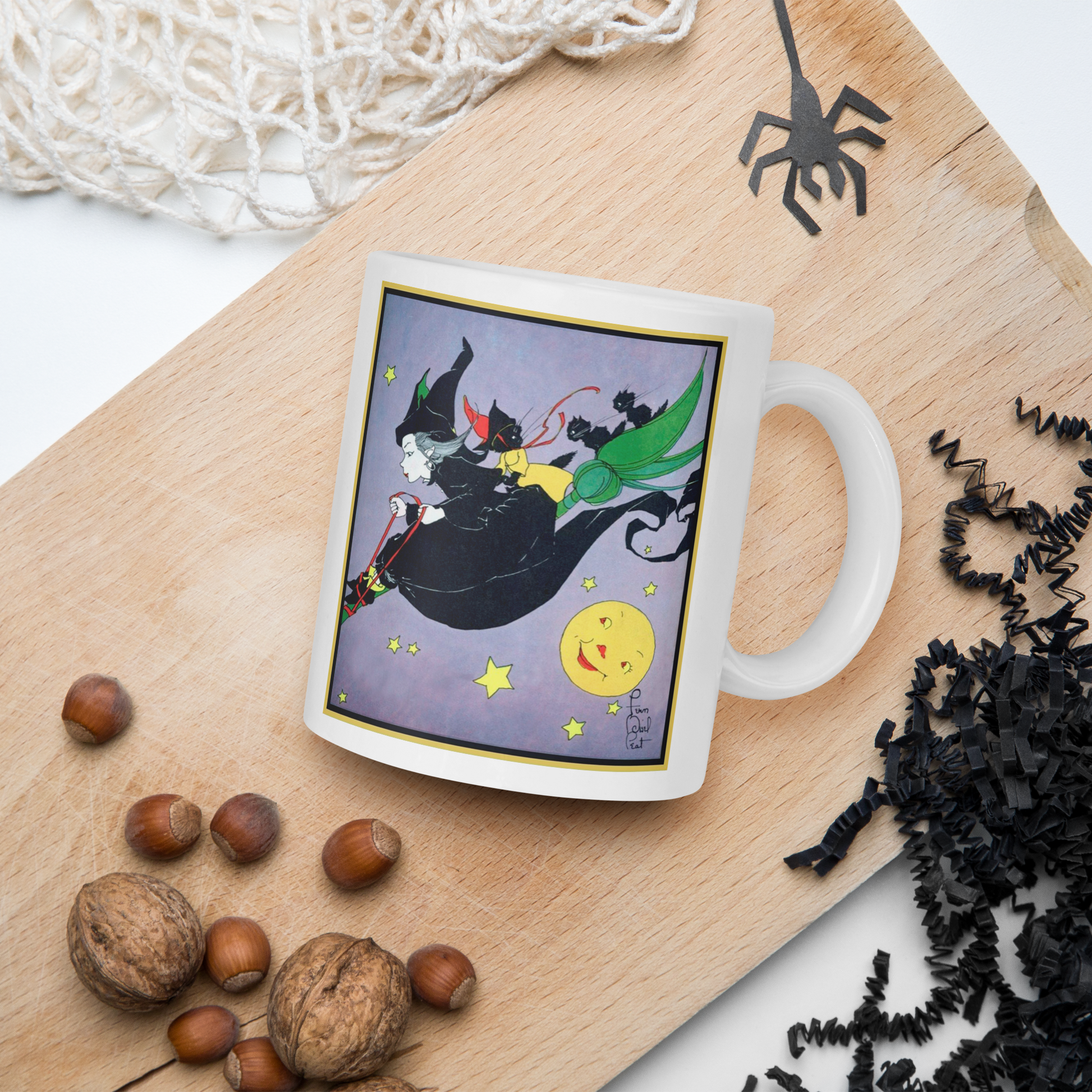 This ceramic glossy mug features a vintage Halloween illustration by Fern Bisel Peat. It features a witch dressed in all black soaring through the air on her broom with black cats. There is a smiling full yellow moon.