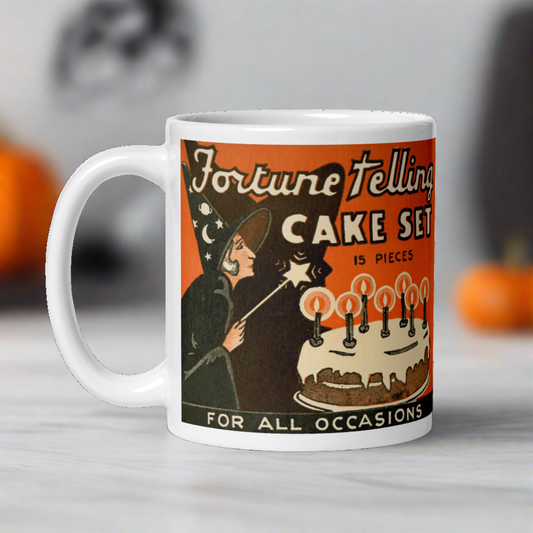 This ceramic glossy mug features a retro vintage Halloween Print of a Fortune Telling Cake Set. It features the artwork of a witch waving a magic star wand over a cake with glowing candles.