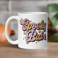 This ceramic glossy coffee mug features cursive lettering that says Spooky Babe. The colors are pastel pinks and yellows and have stars.