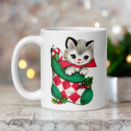 This ceramic glossy coffee mug features a retro vintage Midcentury illustration of an adorable kitten wearing a red bow and is in a stocking with a candy cane.