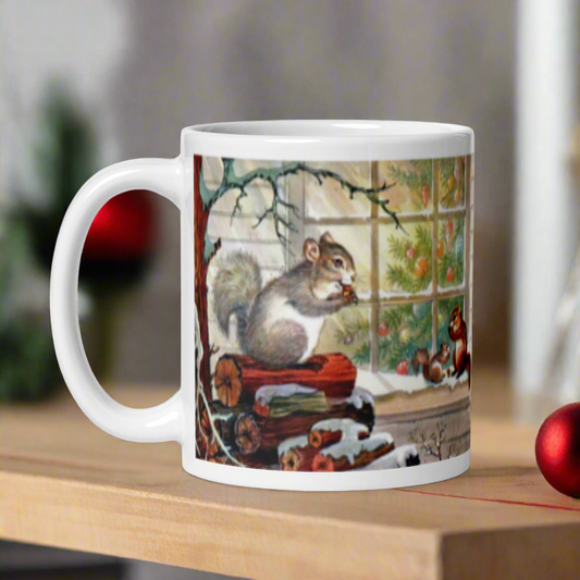 This ceramic glossy coffee mug features a squirrel family of three snacking on some acorns outside in the snow. One is perched on a pile of logs and the smaller two are on a window sill. Inside the window you can see a beautiful Christmas tree.