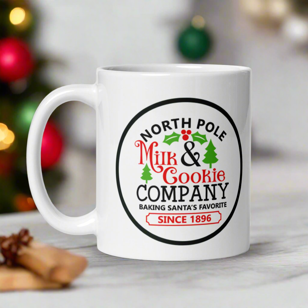 This ceramic glossy coffee mug says North Pole Milk and Cookie Company Baking Santa's Favorite Since 1896. It features little green trees and holly leaves and berries.