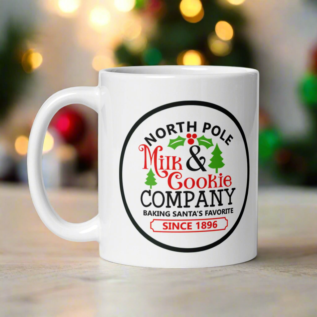 This ceramic glossy coffee mug says North Pole Milk and Cookie Company Baking Santa's Favorite Since 1896. It features little green trees and holly leaves and berries.