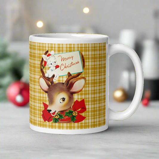 This ceramic glossy coffee mug features a retro vintage illustration of a reindeer wearing a red bow with bells and holly. There is a white bunny sitting in her antlers wearing a santa hat and mittens holding a card that says Merry Christmas.