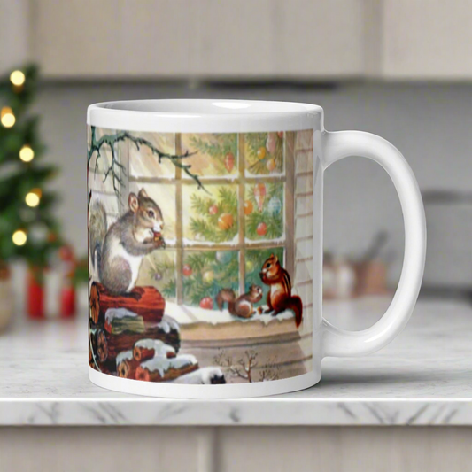 This ceramic glossy coffee mug features a squirrel family of three snacking on some acorns outside in the snow. One is perched on a pile of logs and the smaller two are on a window sill. Inside the window you can see a beautiful Christmas tree.