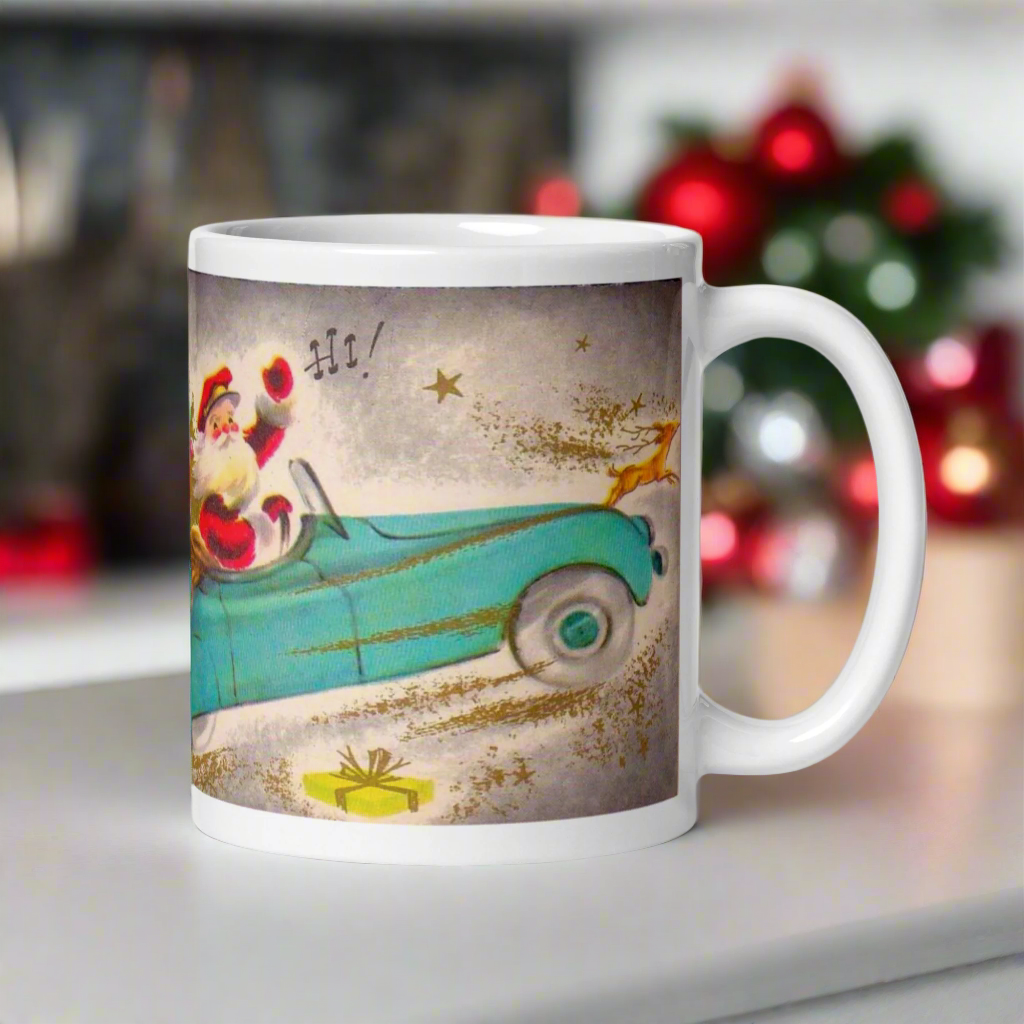 This ceramic glossy coffee mug features a midcentury Christmas illustration of Santa in a teal blue car convertible with a christmas tree in the back seat, the car is pulling his pink sleigh of presents.