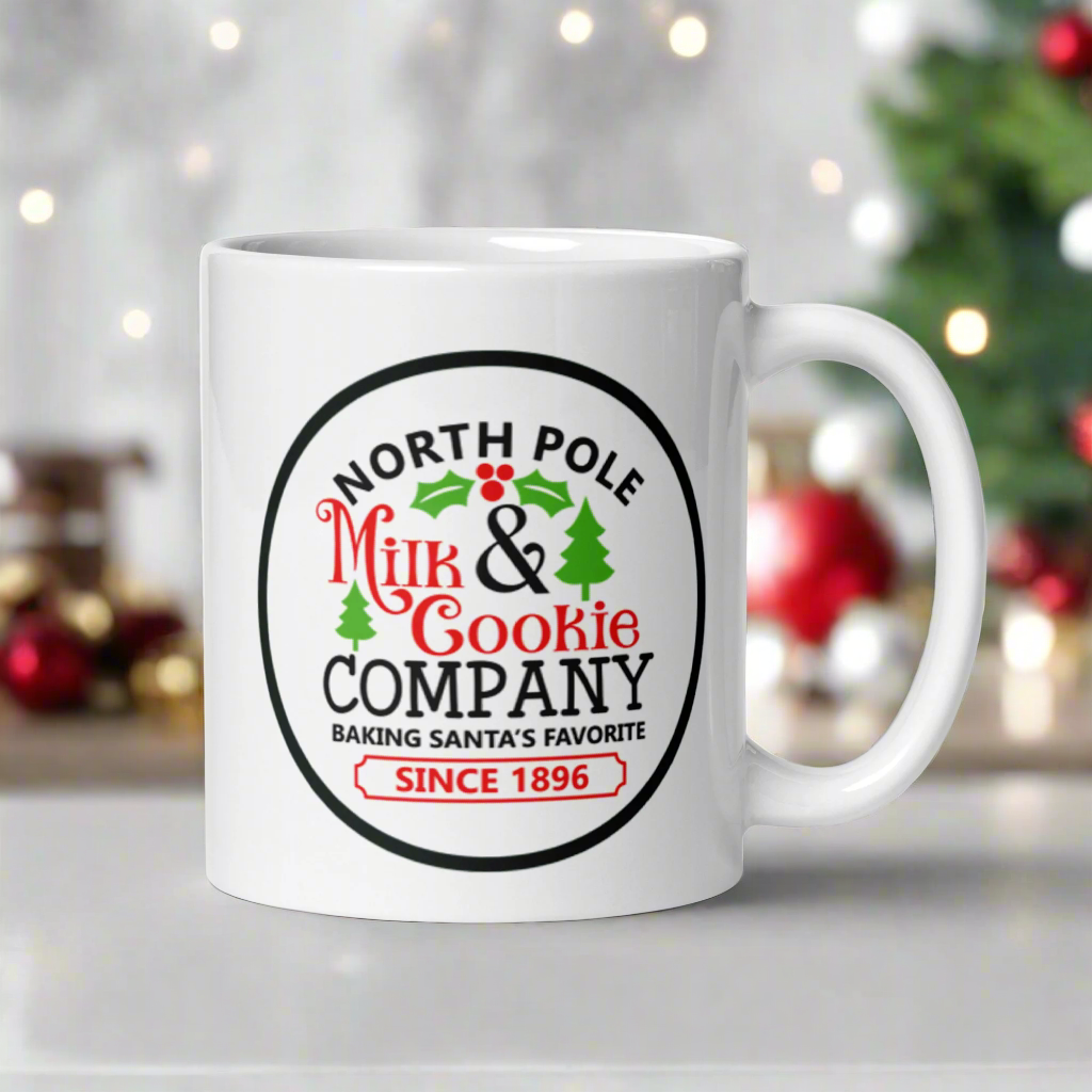 This ceramic glossy coffee mug says North Pole Milk and Cookie Company Baking Santa's Favorite Since 1896. It features little green trees and holly leaves and berries.