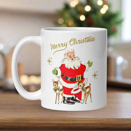 This ceramic glossy coffee mug features Midcentury retro Christmas artwork of a winking Santa wearing green gloves with two baby reindeer. The reindeer are wearing green bows and one is holding Santa's hat in her mouth. There are gold stars and lettering that says Merry Christmas.