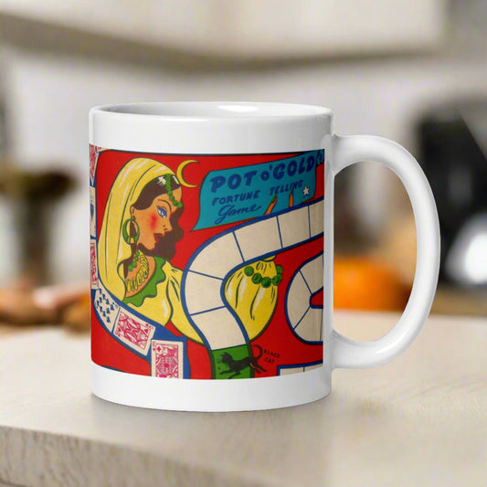 This ceramic glossy coffee mug features a vintage Halloween illustration of a Pot O'Gold Fortune Telling Game. It features a celestial fortune teller dressed in yellow with cards and a board game path.