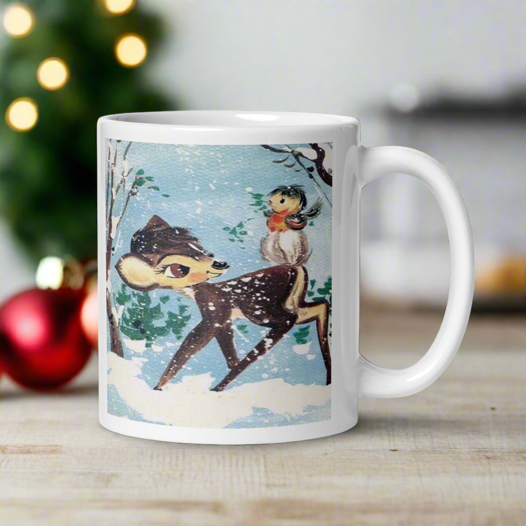 This glossy ceramic coffee cup features a retro woodland style Christmas winter illustration of a baby deer in the snow with a cute red and brown bird perched on her tail.