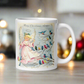 This ceramic glossy coffee mug features a retro Midcentury Christmas illustration of an angel dressed in pink directing blue, yellow and pink songbirds. At the top it says Merry Christmas HONEY