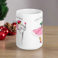 This ceramic glossy coffee mug features a retro vintage Christmas illustration of a woman holding a holly plant checking her mailbox. She is wearing a pink hat, pink and white striped dress, and pink heels. The illustration says A Christmas Note.