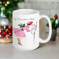 This ceramic glossy coffee mug features a retro vintage Christmas illustration of a woman holding a holly plant checking her mailbox. She is wearing a pink hat, pink and white striped dress, and pink heels. The illustration says A Christmas Note.