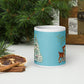 This glossy ceramic coffee mug features 
 Midcentury vintage artwork of an adorable reindeer with holly in her mouth, bunnies, and a Christmas Tree. There is gold lettering that says Season's Greetings and a blue felt background.