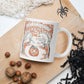 This glossy ceramic coffee mug features a retro vintage Halloween illustration that says Halloween with trees with spooky cute faces and orange leaves, with a jack o lantern in the middle and a black cat sleeping on the pumpkin.