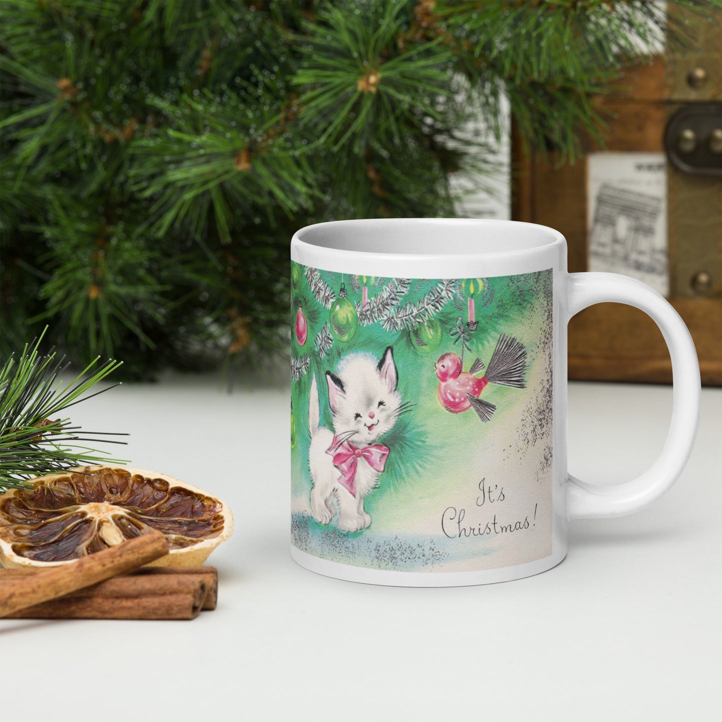 This ceramic glossy coffee mug features a midcentury vintage Christmas Illustration that says It's Christmas! There is an adorable white kitten wearing a pink bow underneath the christmas tree.